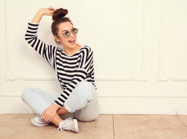 Genç güzel esmer kadın kız modeli yaz hipster giysileri güneş gözlüğü duvarının yakınında poz çıplak makyaj ile portresi. Katta oturan