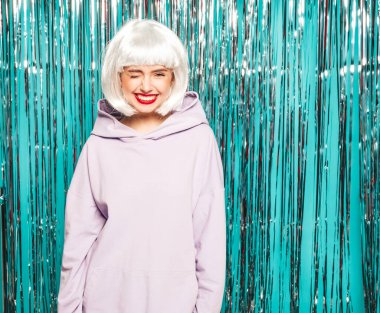 Beyaz peruklu ve kırmızı dudaklı genç seksi hippi kız. Yaz kıyafetleri içinde güzel, modaya uygun bir kadın. Stüdyoda mavi parlak parlak arka planda poz veren üzgün bir model.