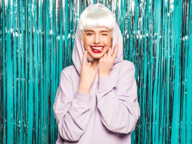 Beyaz peruklu ve kırmızı dudaklı genç seksi hippi kız. Yaz kıyafetleri içinde güzel, modaya uygun bir kadın. Stüdyoda mavi parlak parlak arka planda poz veren tasasız bir model.