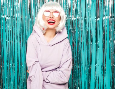 Beyaz peruklu ve kırmızı dudaklı genç seksi hippi kız. Yaz kıyafetleri içinde güzel, modaya uygun bir kadın. Stüdyoda mavi parlak parlak arka planda poz veren tasasız bir model.