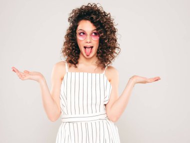 Kıvırcık saçlı güzel bir mankenin portresi yaz hippi kıyafetleri giymiş tasasız bir kız her iki elinde de benzer bir ürün seçimi için bir şeyler sergiliyor.