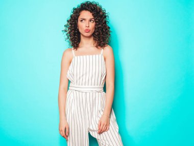 Kıvırcık saçlı, güzel bir mankenin portresi yaz hippi kıyafetleri içinde. Mavi duvarın yanındaki stüdyoda poz veren kaygısız kız. Moda, komik ve pozitif kadın.