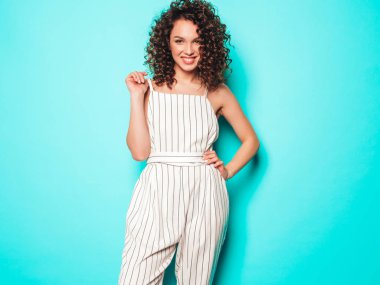 Kıvırcık saçlı, güzel bir mankenin portresi yaz hippi kıyafetleri içinde. Mavi duvarın yanındaki stüdyoda poz veren kaygısız kız. Moda, komik ve pozitif kadın.