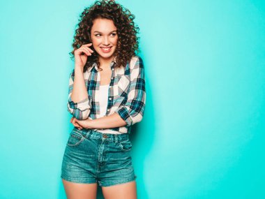 Kıvırcık saçlı, güzel bir mankenin portresi yaz hippi kıyafetleri içinde. Mavi duvarın yanındaki stüdyoda poz veren kaygısız kız. Moda, komik ve pozitif kadın.