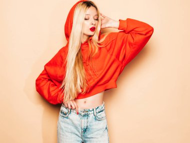 Moda kırmızı kapüşonlu ve burnunda küpeli genç güzel hippi kötü kız portresi. Stüdyoda poz veren kaygısız, güler yüzlü sarışın kadın. Pozitif model eğleniyor. 