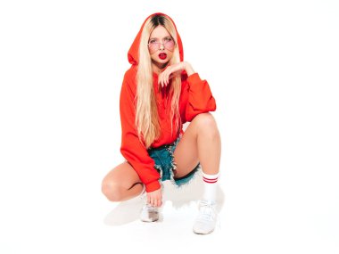 Moda kırmızı kapüşonlu kötü kız ve burnunda küpe olan genç, güzel hippi kız portresi. Stüdyoda oturan kaygısız, güler yüzlü sarışın kadın. Pozitif model. Beyazlar üzerinde izole edilmiş.