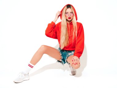 Moda kırmızı kapüşonlu kötü kız ve burnunda küpe olan genç, güzel hippi kız portresi. Stüdyoda oturan kaygısız, güler yüzlü sarışın kadın. Pozitif model. Beyazlar üzerinde izole edilmiş.