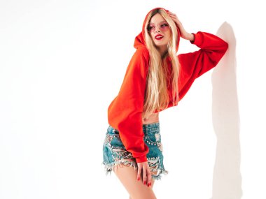 Moda kırmızı kapüşonlu kötü kız ve burnunda küpe olan genç güzel hippi portresi. Stüdyoda poz veren kaygısız, güler yüzlü sarışın kadın. Pozitif model. Beyazlar üzerinde izole edilmiş. 