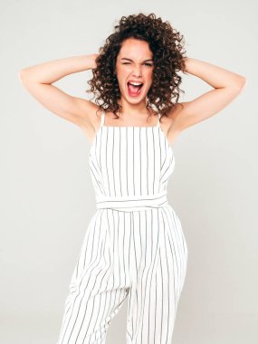 Kıvırcık saçlı, güzel bir mankenin portresi yaz hippi kıyafetleri giymiş, gri arka planda poz veren kaygısız bir kız. Son moda komik ve pozitif kadın.