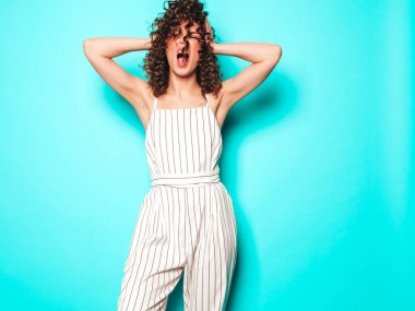 Kıvırcık saçlı, güzel bir mankenin portresi yaz hippi kıyafetleri içinde. Mavi duvarın yanındaki stüdyoda poz veren kaygısız kız. Moda, komik ve pozitif kadın.