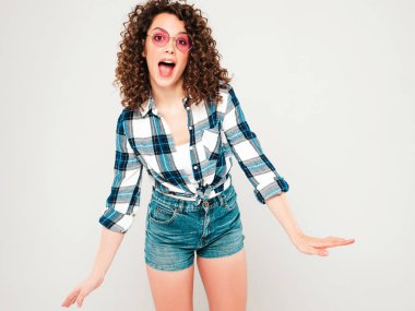 Kıvırcık saçlı, güzel bir mankenin portresi yaz hippi kıyafetleri giymiş, gri arka planda poz veren kaygısız bir kız. Son moda komik ve pozitif kadın.