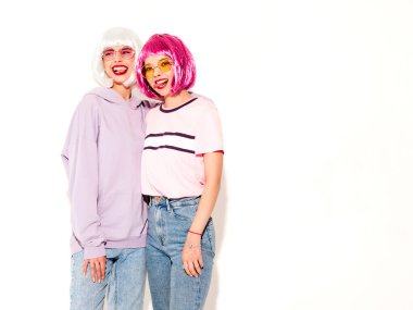 Two young sexy smiling hipster girls in wigs and red lips.Beautiful trendy women in summer clothes.Carefree models posing near white wall in studio.Positive female going crazy and hugging