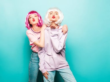 İki seksi gülümseyen hippi kız peruk ve kırmızı dudak. Yaz kıyafetleri içinde güzel moda kadınlar. Stüdyoda mavi duvarın yanında poz veren tasasız mankenler.