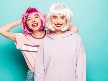 Peruklu ve kırmızı dudaklı iki genç seksi hippi kız. Yaz kıyafetleri içinde güzel moda kadınlar. Stüdyoda mavi duvarın yanında poz veren tasasız mankenler. 