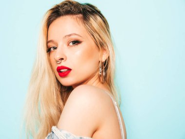 Genç, güzel, hippi kötü kız portresi moda kotlar içinde, yaz kıyafetleri içinde ve burnunda küpe ile stüdyoda poz veren kaygısız, güler yüzlü sarışın kadın. Pozitif model eğleniyor.