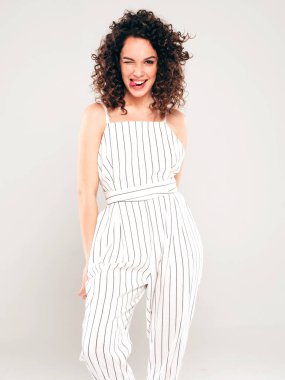 Kıvırcık saçlı güzel bir mankenin portresi yaz hippi kıyafetleri içinde giyinmiş kaygısız bir kız stüdyoda gri arka planda poz veriyor.