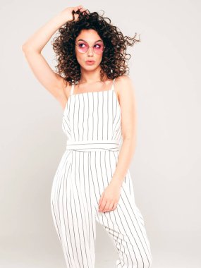 Kıvırcık saçlı, güzel bir mankenin portresi yaz hippi kıyafetleri giymiş, gri arka planda poz veren kaygısız bir kız. Son moda komik ve pozitif kadın.