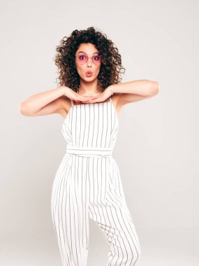 Kıvırcık saçlı, güzel bir mankenin portresi yaz hippi kıyafetleri giymiş, gri arka planda poz veren kaygısız bir kız. Son moda komik ve pozitif kadın.