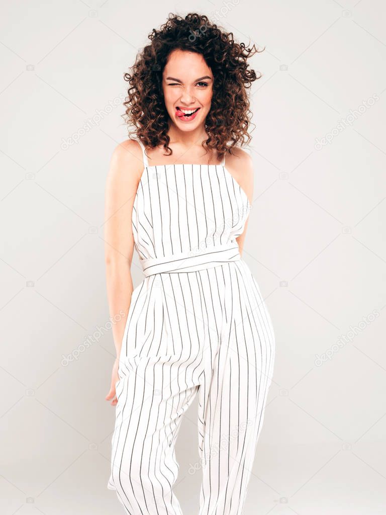 Portrait of beautiful smiling model with afro curls hairstyle dressed in summer hipster clothes.Sexy carefree girl posing in studio on gray background.Trendy funny and positive woman shows tongue