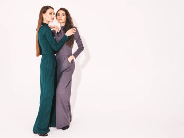 Stüdyoda beyaz duvarın yanında poz veren kaygısız kadınlar. Parlak makyajlı moda mankenler. Sarılıp birbirlerine dokunuyorlar.
