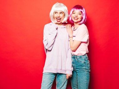 Two young sexy smiling hipster girls in white wigs and red lips.Beautiful trendy women in summer clothes.Carefree models posing near red wall in studio.Positive female going crazy