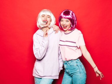 Two young sexy smiling hipster girls in white wigs and red lips.Beautiful trendy women in summer clothes.Carefree models posing near red wall in studio.Positive female going crazy