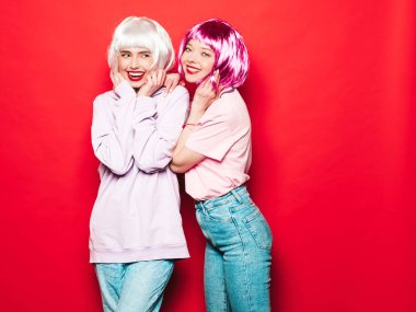 Two young sexy smiling hipster girls in white wigs and red lips.Beautiful trendy women in summer clothes.Carefree models posing near red wall in studio.Positive female going crazy