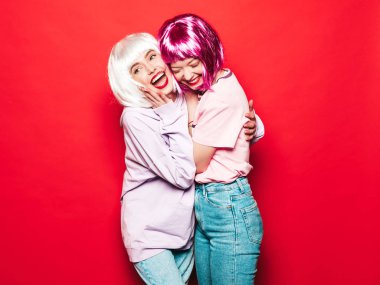 Two young sexy smiling hipster girls in white wigs and red lips.Beautiful trendy women in summer clothes.Carefree models posing near red wall in studio.Positive female going crazy