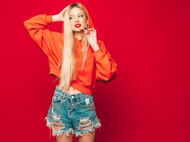 Moda kırmızı kapüşonlu kötü kız ve burnunda küpe olan genç, güzel hippi kız portresi. Stüdyoda poz veren kaygısız, güler yüzlü sarışın kadın. Şeker şekerini yalayan pozitif model.