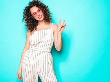 Portrait of beautiful smiling model with afro curls hairstyle dressed in summer hipster clothes.Sexy carefree girl posing near blue wall.Trendy funny and positive woman