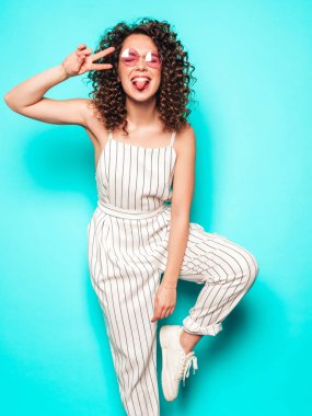 Portrait of beautiful smiling model with afro curls hairstyle dressed in summer hipster clothes.Sexy carefree girl posing near blue wall.Trendy funny and positive woman