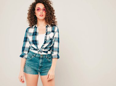 Kıvırcık saçlı, güzel bir mankenin portresi yaz hippi kıyafetleri giymiş, gri arka planda poz veren kaygısız bir kız. Son moda komik ve pozitif kadın.