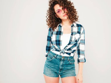 Kıvırcık saçlı, güzel bir mankenin portresi yaz hippi kıyafetleri giymiş, gri arka planda poz veren kaygısız bir kız. Son moda komik ve pozitif kadın.