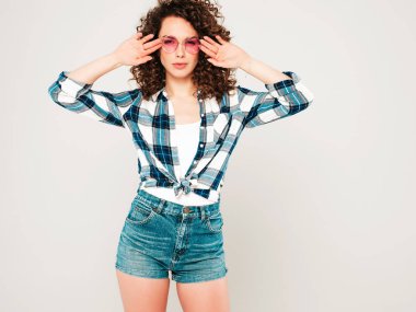 Kıvırcık saçlı, güzel bir mankenin portresi yaz hippi kıyafetleri giymiş, gri arka planda poz veren kaygısız bir kız. Son moda komik ve pozitif kadın.