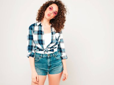 Kıvırcık saçlı, güzel bir mankenin portresi yaz hippi kıyafetleri giymiş, gri arka planda poz veren kaygısız bir kız. Son moda komik ve pozitif kadın.