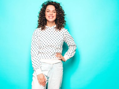 Kıvırcık saçlı, güzel bir mankenin portresi yaz hippi kıyafetleri giymiş, mavi duvarın yanında poz veren kaygısız bir kız. Beyaz kapüşonlu, modaya uygun ve pozitif bir kadın.