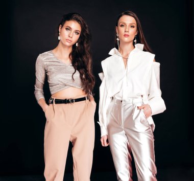 Güzel moda yaz kıyafetleri içinde iki güzel esmer kız. Stüdyoda siyah arka planda poz veren kaygısız kadınlar. Parlak akşam makyajlı, modaya uygun mankenler.