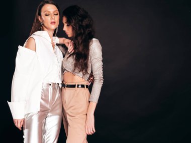 Güzel moda yaz kıyafetleri içinde iki güzel esmer kız. Stüdyoda siyah arka planda poz veren kaygısız kadınlar. Parlak akşam makyajlı, modaya uygun mankenler.