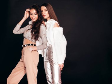 Güzel moda yaz kıyafetleri içinde iki güzel esmer kız. Stüdyoda siyah arka planda poz veren kaygısız kadınlar. Parlak akşam makyajlı, modaya uygun mankenler.