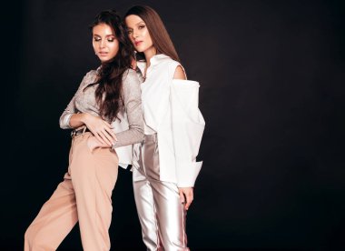 Güzel moda yaz kıyafetleri içinde iki güzel esmer kız. Stüdyoda siyah arka planda poz veren kaygısız kadınlar. Parlak akşam makyajlı, modaya uygun mankenler.