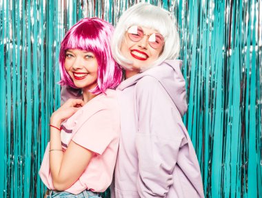 Two young sexy smiling hipster girls in white wigs and red lips.Beautiful trendy women in summer clothes.Carefree models posing on blue silver shiny tinsel background in studio.Positive female