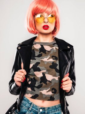 Siyah deri ceketli ve burnunda küpesi olan genç, güzel hippi kötü bir kızın portresi. Gri duvarın yanında pembe perukla stüdyoda oturan kaygısız, güler yüzlü bir kadın. Güneş gözlüklü, kendine güvenen bir model.