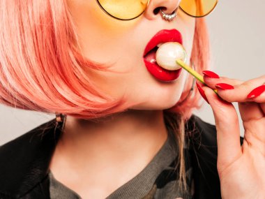 Kapalı dudaklı, genç, güzel hippi kötü kız modaya uygun siyah deri ceketli ve burnunda küpe olan. Stüdyoda pembe perukla poz veren kaygısız, güler yüzlü kadın. Şekeri yalayan pozitif model.