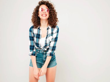 Kıvırcık saçlı, güzel bir mankenin portresi yaz hippi kıyafetleri giymiş, gri arka planda poz veren kaygısız bir kız. Son moda komik ve pozitif kadın.