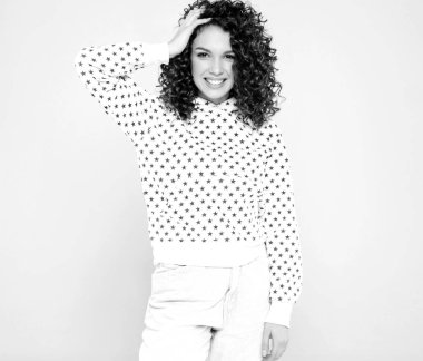 Kıvırcık saçlı, güzel bir mankenin portresi yaz hippi kıyafetleri içinde. Gri arka planda poz veren kaygısız bir kız. Beyaz kapüşonlu, modaya uygun ve pozitif bir kadın.