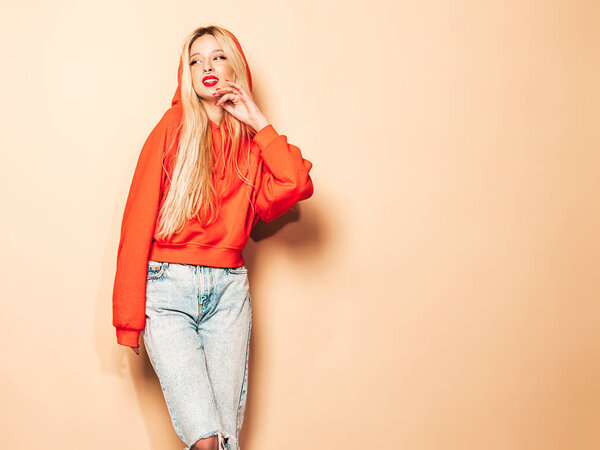 Portrait of young beautiful hipster bad girl in trendy red summer hoodie and earring in her nose.Sexy carefree smiling blond woman posing in studio.Positive model