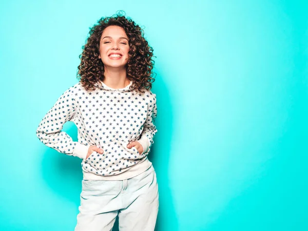 Portrait of beautiful smiling model with afro curls hairstyle dressed in summer hipster clothes.Sexy carefree girl posing near blue wall.Trendy funny and positive woman in white hoodie