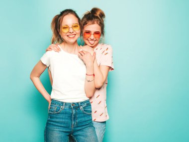 İki güzel sarışın, gülümseyen yenilikçi kız, son moda hippi kot pantolon giyiyorlar. Mavi duvarın yanında poz veren kaygısız seksi kadınlar. Moda ve pozitif modeller eğleniyor. Dillerini gösteriyorlar.