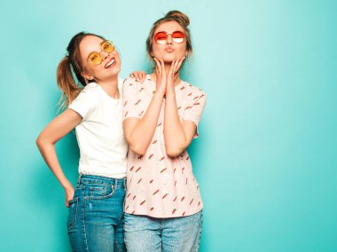 İki güzel sarışın, gülümseyen yenilikçi kız, son moda hippi kot pantolon giyiyorlar. Mavi duvarın yanında poz veren kaygısız seksi kadınlar. Moda ve pozitif modeller eğleniyor.