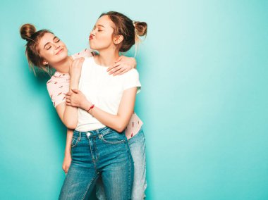 İki güzel sarışın, gülümseyen yenilikçi kız, son moda hippi kot pantolon giyiyorlar. Mavi duvarın yanında poz veren kaygısız seksi kadınlar. Moda ve pozitif modeller eğleniyor.